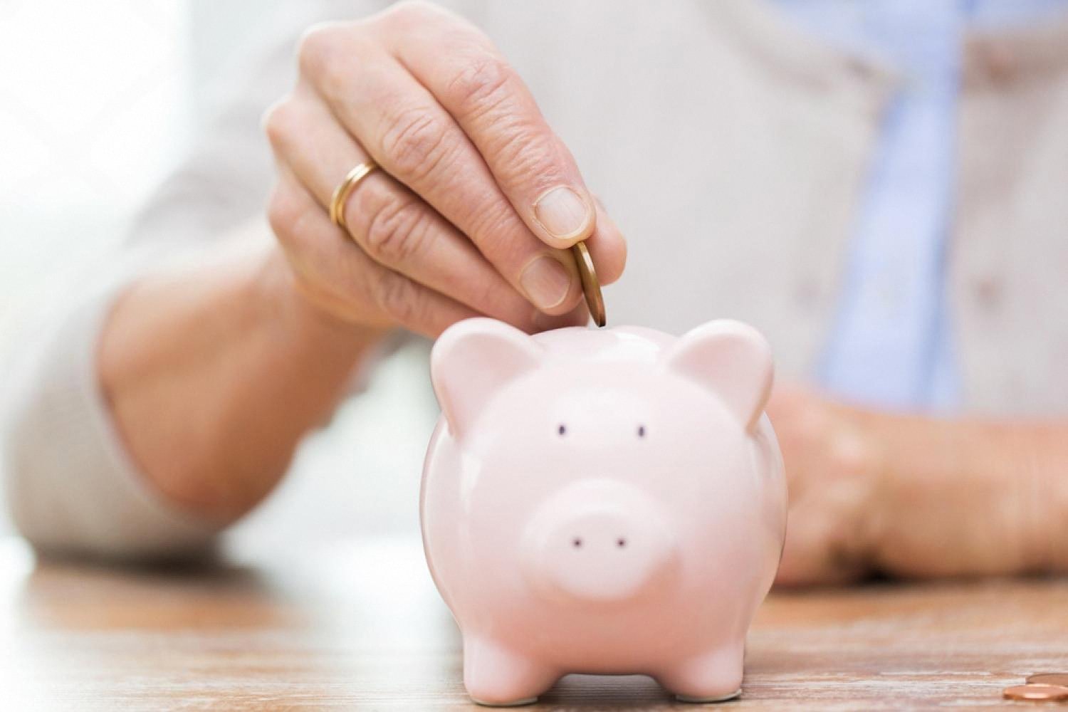 Hand placing a coin into a pink piggy bank, saving for an emergency fund