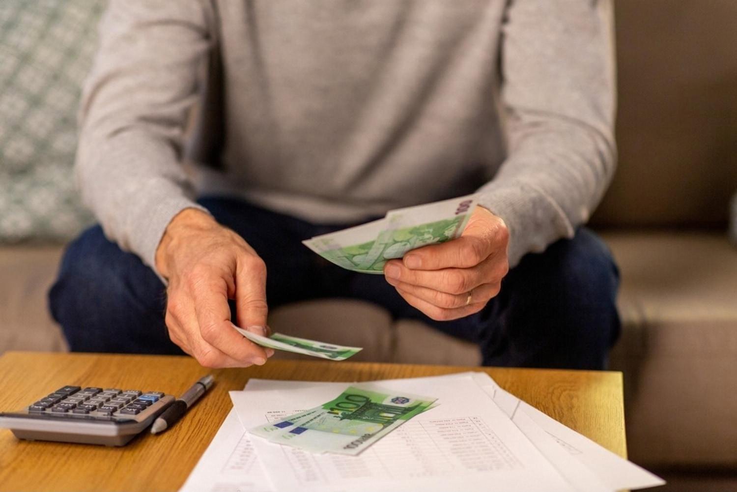 Man counting cash with a calculator and bills, reviewing household budget in the UAE