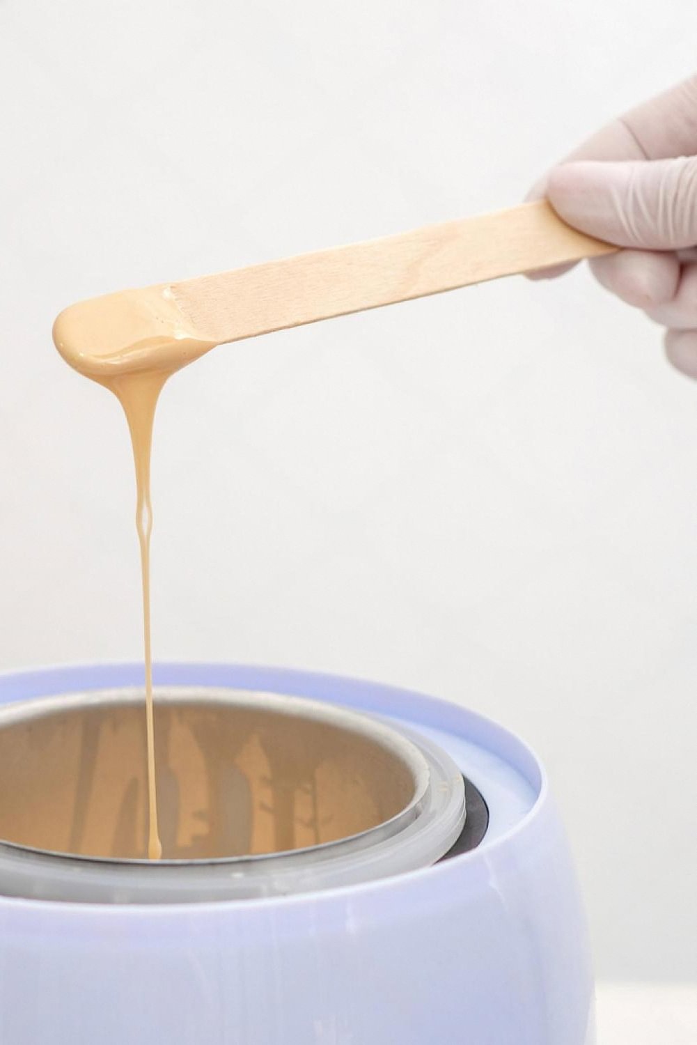 Warm sugar wax dripping from a wooden spatula into a heated pot at a UAE beauty salon